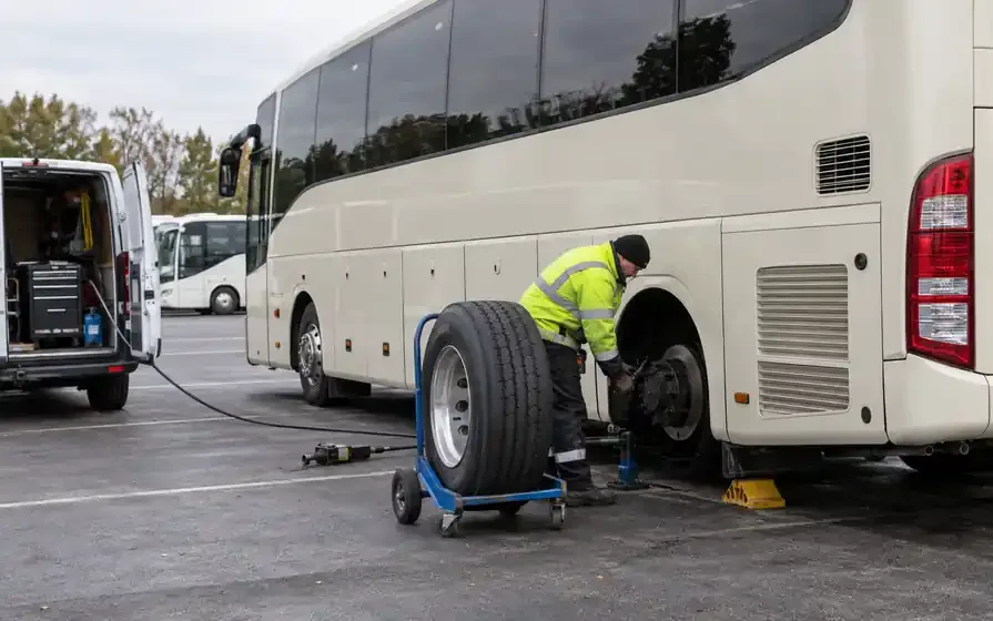 Mobile technician fitting a rear tyre on a cream touring coach.